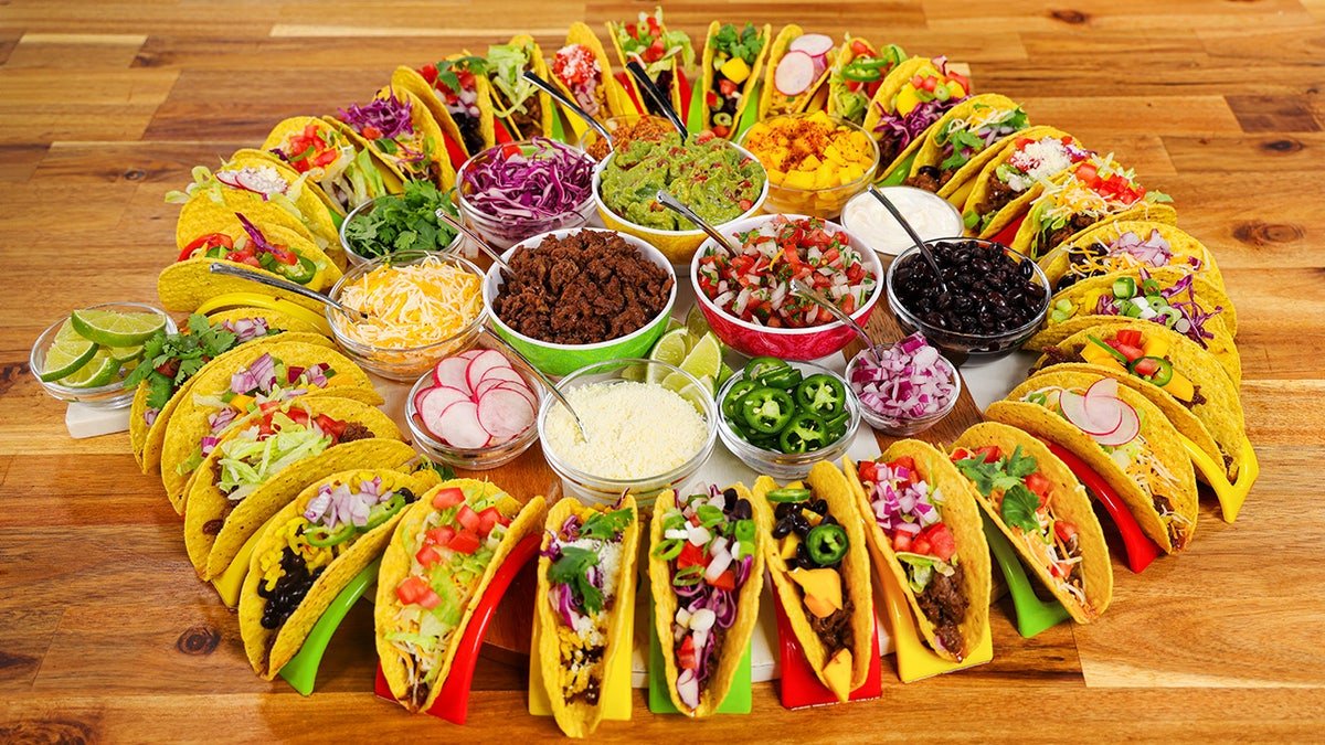 A taco board consisting of a circle of filled hard taco shells with various taco tops in the middle. 