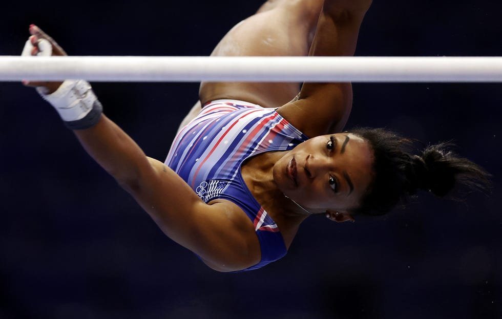 Gymnast simone jumps up and down in the air as she looks towards one of the uneven bars