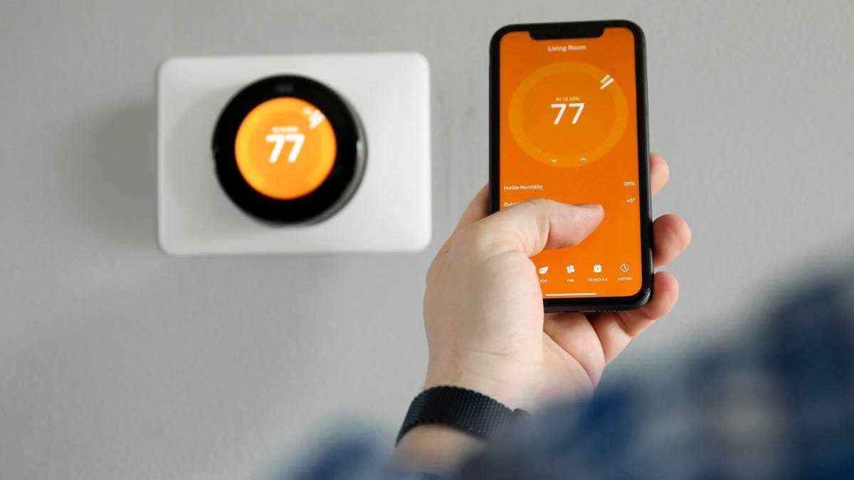 A person holds a phone in front of a smart thermostat.